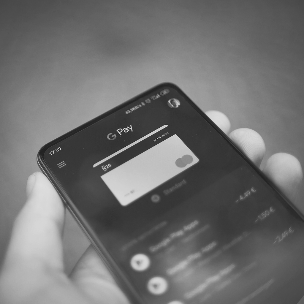 Black & white image depicting someone making a payment with Google Pay on a mobile device